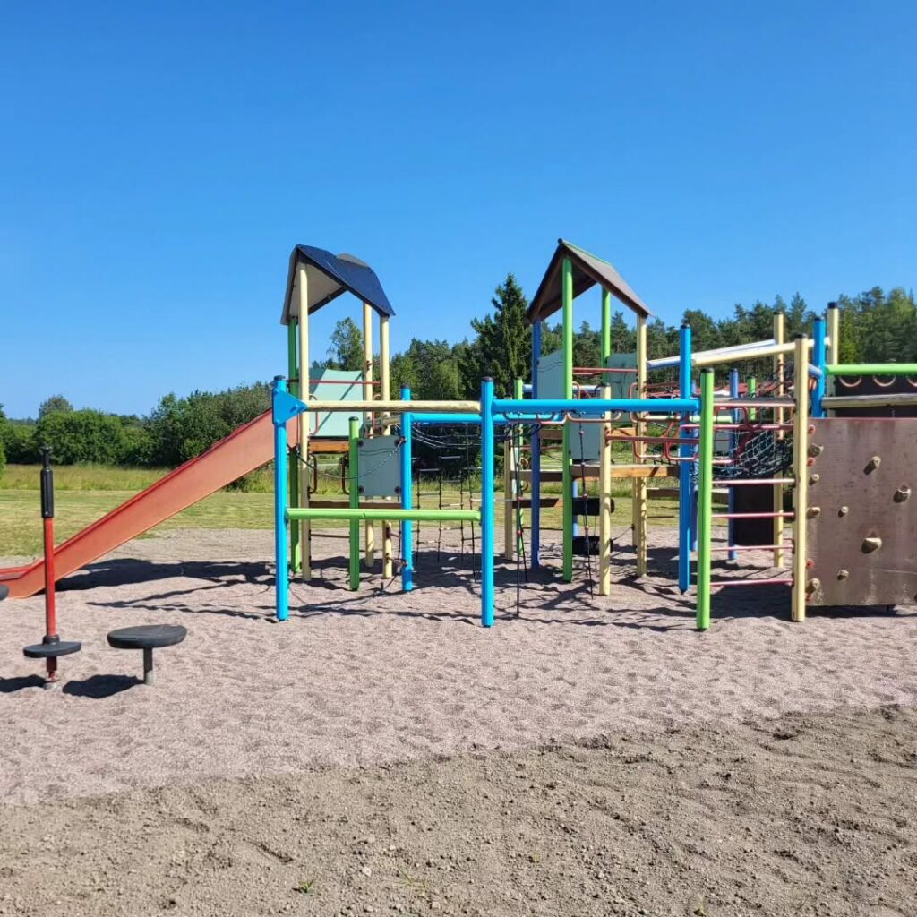 Lekparken med rutschkana och klätterställning, allt på mjuk sand.